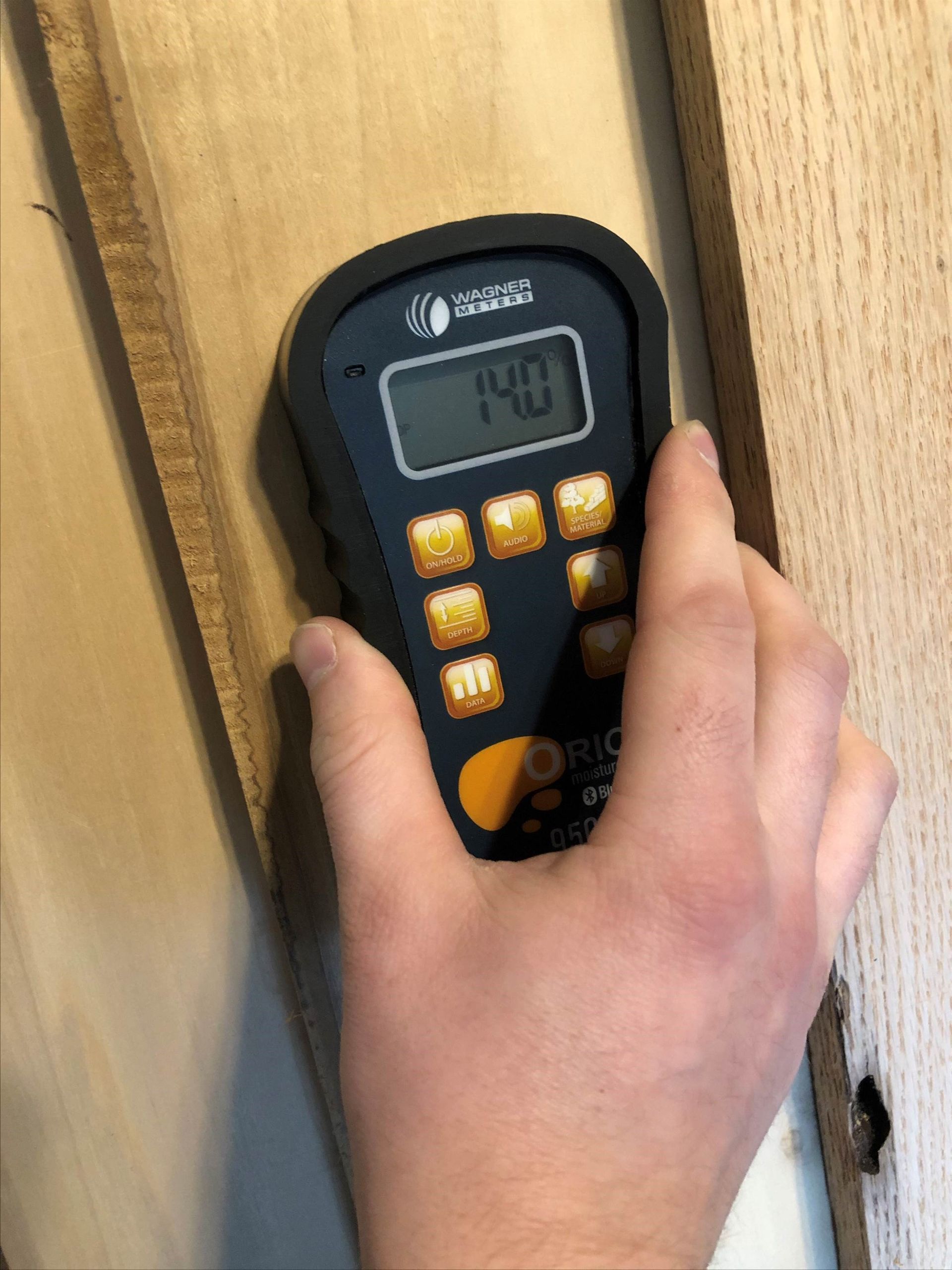 A hand holding a wood moisture meter against a board